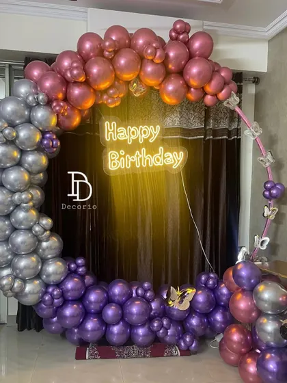 A detailed look at the circular balloon arch for a birthday celebration. The arrangement features metallic purple, silver, and rose gold balloons with small butterfly accents for a touch of whimsy.