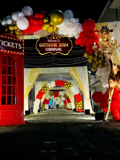 A slightly different angle of the nighttime carnival entrance, showing the glowing lights and balloon arrangements.