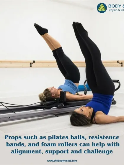 Two clients perform a synchronized leg lift on the Reformer, demonstrating how props can aid in maintaining form and alignment.