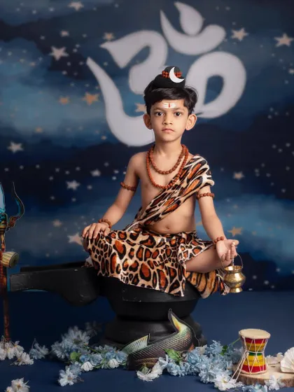 A powerful portrait of a young boy as Lord Shiva, holding a trishul and sitting in a meditative pose.