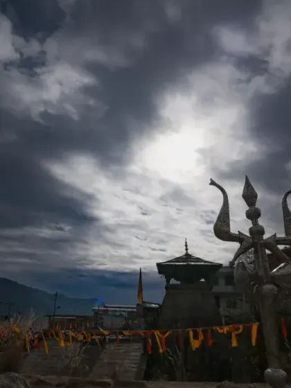 A dramatic wide-angle shot of the temple's trishul against a cloudy sky, capturing the powerful and spiritual energy of the location.