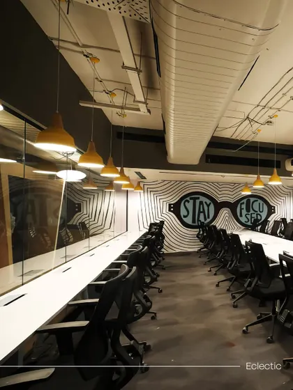 A long, shared workspace at Innov8 with a bold 'Stay Focused' mural at the end. The perspective lines of the desk and lighting draw the eye, emphasizing the room's purpose.