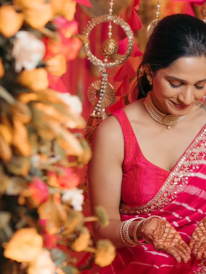 A beautiful, candid portrait of the bride looking down at her simple yet elegant mehndi design. The vibrant floral background adds to the festive feel of the ceremony.