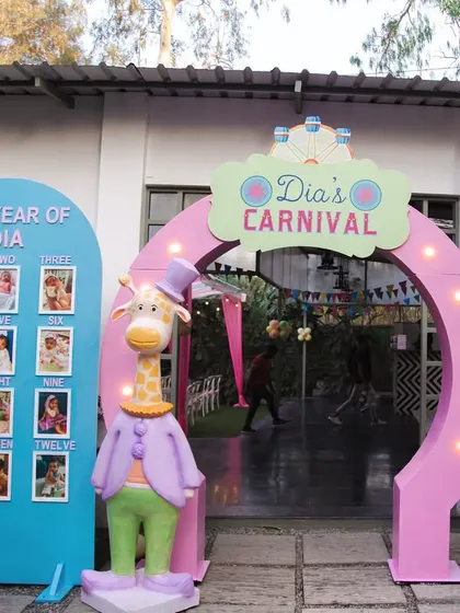 The entrance to Dia's Carnival, featuring a personalized archway, a milestone board celebrating her first year, and a dapper giraffe character to welcome guests.