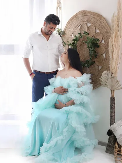 A full-length view of a couple in our bright, bohemian-themed studio corner. The mother-to-be is seated in a beautiful ruffled gown, creating a soft and romantic portrait.
