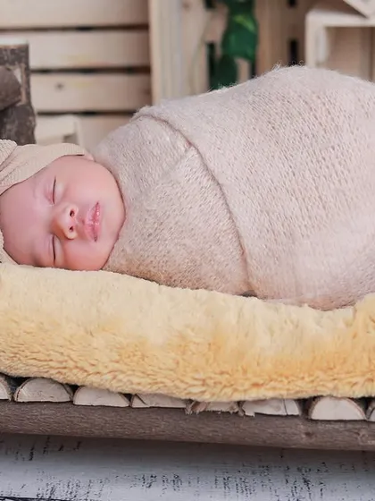 A close-up of the baby sleeping on the rustic log bed, wrapped in a neutral-toned swaddle. The textures of the wood and soft bedding create a lovely contrast.