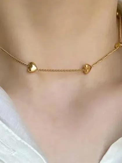 A model wearing the delicate gold-toned necklace with small heart charms, showing how it sits beautifully on the collarbone.