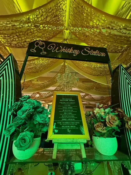 A close-up of a 'Whiskey Station' with a custom menu on an easel, flanked by floral arrangements, showing our attention to personalized details.