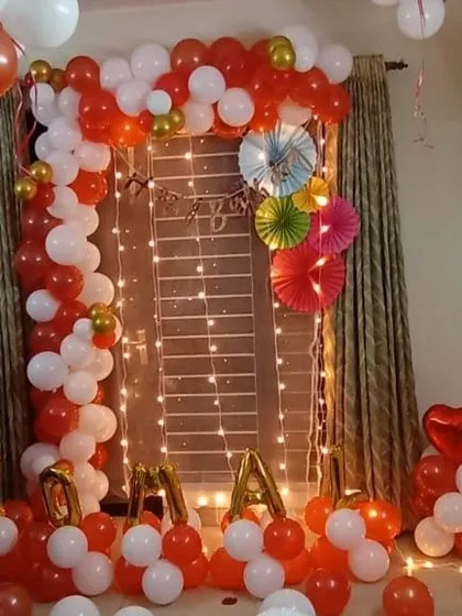 A vibrant red, white, and gold room decoration. This setup features a balloon arch around a window, accented with fairy lights and paper fans, perfect for a festive home party.