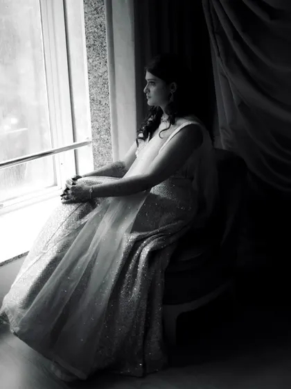 A pensive black and white portrait of the bride looking out a window, lost in thought.