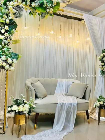 A sophisticated Roka setup with a C-shaped arch of white flowers and tropical leaves. The hanging lights and gold-accented floral stands add a touch of luxury and modernity.
