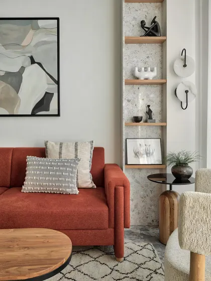 A close-up of the living area in Apartment 1101. The rust-colored sofa is paired with terrazzo shelves adorned with vibrant artifacts, exuding charm and personality.
