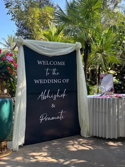 A welcome sign for the wedding of Abhishek and Pramati, elegantly draped and surrounded by colorful flowers.