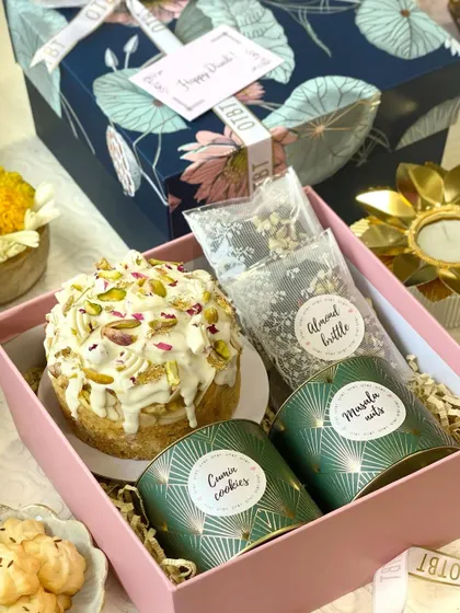 This Diwali hamper combines modern bakes with traditional flavors. It includes a pistachio-crusted tea cake, crunchy almond brittle, savory cumin cookies, and masala nuts, offering a wonderful mix of sweet and savory.