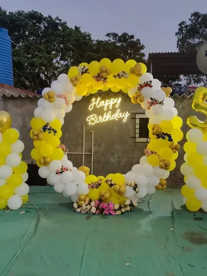 A cheerful yellow and white balloon ring for a 5th birthday, set up on a rooftop and decorated with small flowers.
