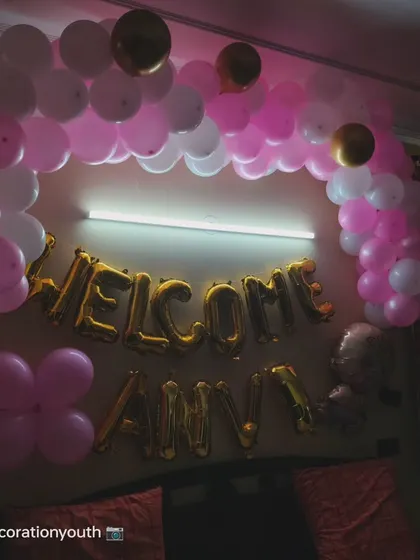 A sweet "Welcome Anvi" decoration. This bedroom setup features a pink and white balloon arch over the bed with the name in gold foil letters.