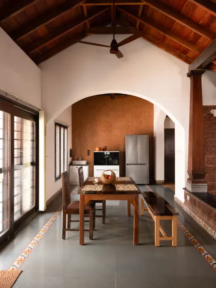 A view of the dining hall in our Vinaya residence project. This space is defined by an arch leading to the kitchen, a high vaulted wooden ceiling, and a Lohi lime plaster accent wall, demonstrating how natural materials create warm and functional living areas.