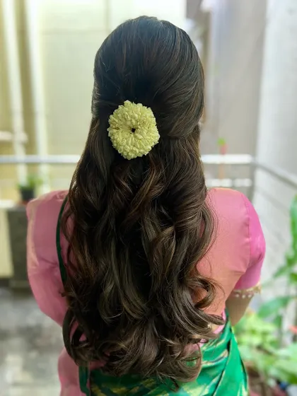 Soft curls and endless elegance. This simple half-up style is adorned with a small jasmine flower arrangement for a touch of traditional grace.