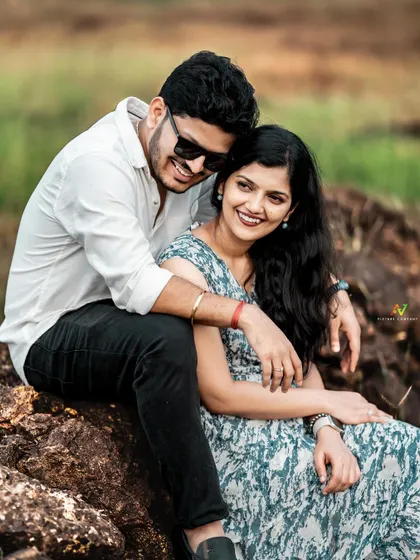 A joyful and candid portrait of a couple in sunglasses, laughing and embracing on a rock.