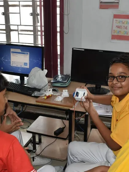 Two students smile for the camera while working on their project at a computer station, demonstrating the fun and engaging nature of our learning environment.
