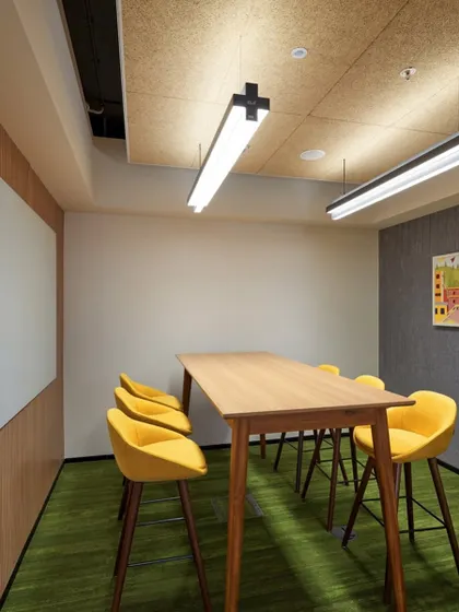 This collaboration space features a high table with yellow stools and a large whiteboard for brainstorming. The wood-fiber acoustic panels on the ceiling help to manage sound.