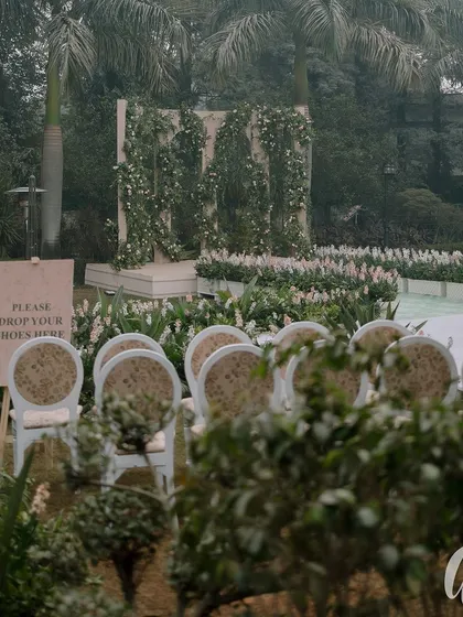 The entrance to the ceremony, with a simple sign asking guests to remove their shoes. The aisle is lined with white flowers, leading to a stage decorated with climbing greenery.
