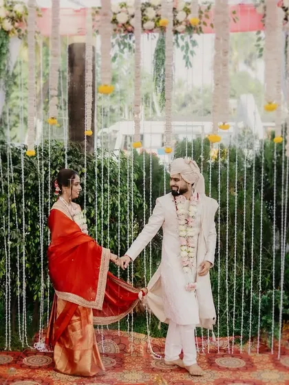 The couple walks hand-in-hand in front of a beautiful floral and curtain backdrop.