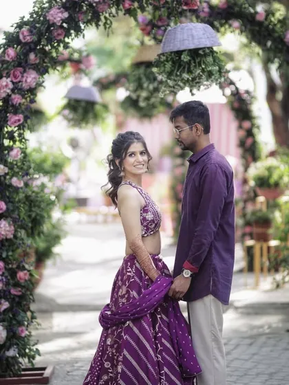 A couple poses under a beautiful floral arch, a perfect shot from their pre-wedding or engagement celebration.