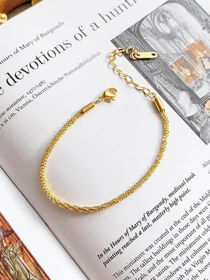 A sparkling, textured gold-toned bracelet resting on a book. This piece has an adjustable clasp to ensure a perfect fit.