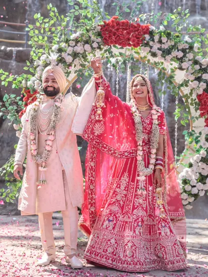 A moment of triumph and joy as the newly married Sikh couple raises their hands in celebration. The shower of petals adds to the festive and happy atmosphere.