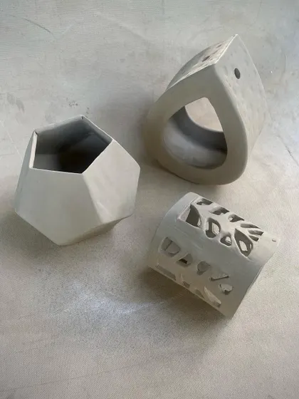 Another angle of the student work from our handbuilding course, showing a hexagonal vase, a teardrop-shaped luminary, and a cylindrical pierced vessel.