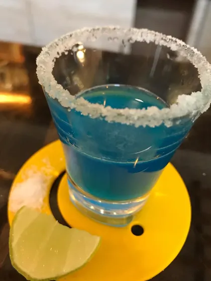 A vibrant blue Kamikaze shot with a sugared rim, ready for a party. We also specialize in creating fun and tasty shots for events.