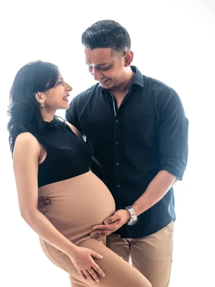 A high-key studio portrait with a pure white background creates a light, airy, and modern feel. This image beautifully highlights the couple's joy and the elegant shape of the baby bump.