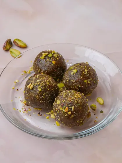 Healthy date and pistachio energy balls, lightly garnished with crushed pistachios on a clear glass plate. This clean shot is perfect for showcasing healthy dessert alternatives or snacks.