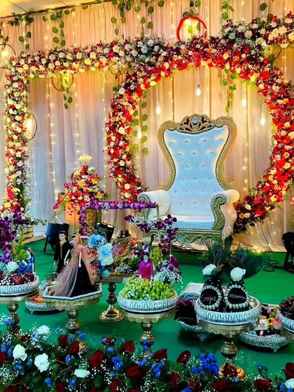 A beautiful baby shower or engagement stage featuring a circular floral arch with hanging lights. The entire setup is brought to life with dozens of my decorated trays, each filled with fruits, sweets, and gifts, all arranged on a green-covered stage.