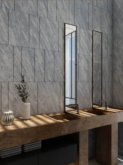 This bathroom design celebrates raw materials and precise detailing. The exposed concrete countertop and grey marble wall tiles create an industrial-minimalist feel, with twin black-framed mirrors adding a strong graphic element.