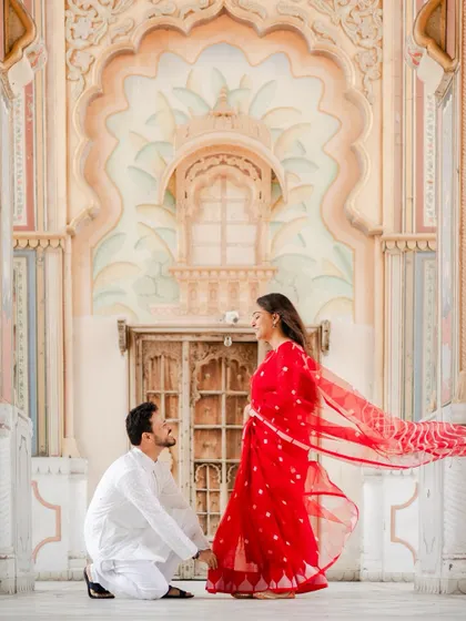 Against the magnificent arches of Jaipur's Patrika Gate, he asked for her forever. The vibrant red of her saree and the grandeur of the setting create a truly royal proposal photograph.