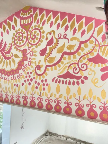 A selfie with a section of the 'Baba's Garden' mural. The combination of gold and pink on the white wall creates a festive and welcoming feel, perfect for this outdoor space.