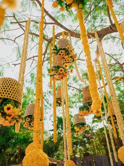 A low-angle shot of the hanging floral baskets and marigold strings, creating a beautiful, textured canopy for the haldi ceremony.