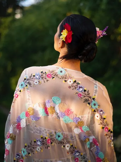 A detail shot of the exquisite, hand-embroidered cape against the light. This image highlights the sheer fabric and the incredible craftsmanship of the piece.