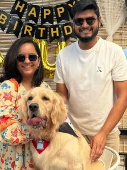 A happy couple poses with their golden retriever in front of "Happy Birthday" balloons. We provide the perfect backdrop for your dog's birthday photos.