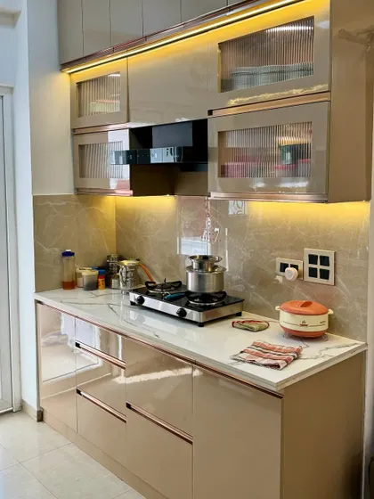 A close-up of the cooking area in this beige kitchen. The design features fluted glass cabinets and rose gold handles for a trendy, elegant look.