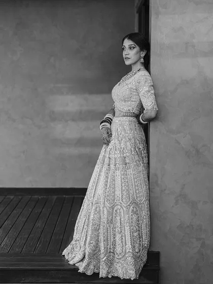 A full-length black and white portrait of a bride leaning against a wall. The simple setting and her graceful pose create a powerful and sophisticated image.
