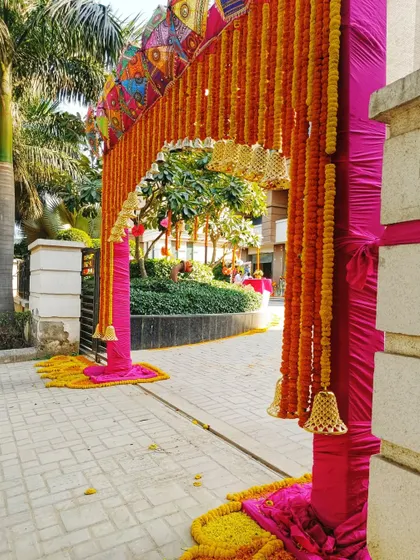 A grand entrance arch for a Mehendi, decorated with marigold garlands, colorful umbrellas, and hanging bells. This sets a festive and traditional tone right from the gate.