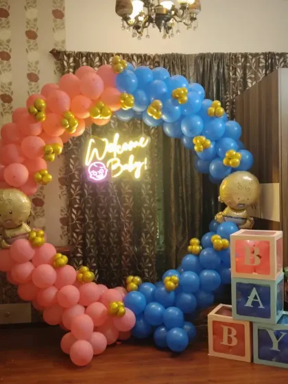 A classic pink and blue theme for a baby shower or gender reveal party. This decoration features a circular balloon arch, a "Welcome Baby" neon sign, and 'BABY' blocks.