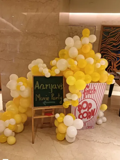 A creative 'Movie Party' entrance decoration. A giant popcorn box made of balloons and a chalkboard sign welcome guests to the celebration.
