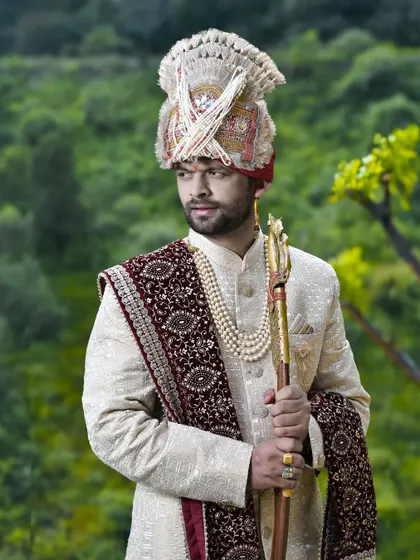 A three-quarter portrait of the groom in his wedding finery. The natural lighting and green background make the colors of his outfit pop.