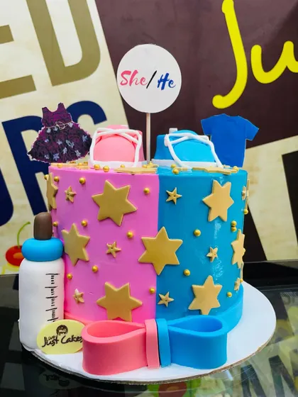 A 2.5kg "She/He" gender reveal cake with pink and blue sides, decorated with baby clothes and a bottle.