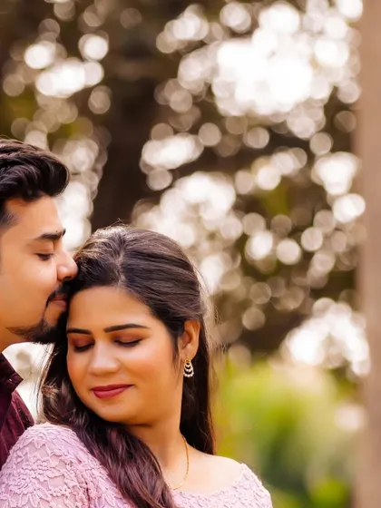 A close-up shot of a tender forehead kiss. The soft, blurry background of the park foliage keeps the focus entirely on the couple's intimate connection.