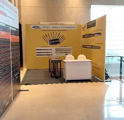 An exhibition booth for Alpha Omega Enterprises, designed to showcase product catalogs and information clearly. The layout includes a small, semi-private meeting desk for discussions with potential clients.